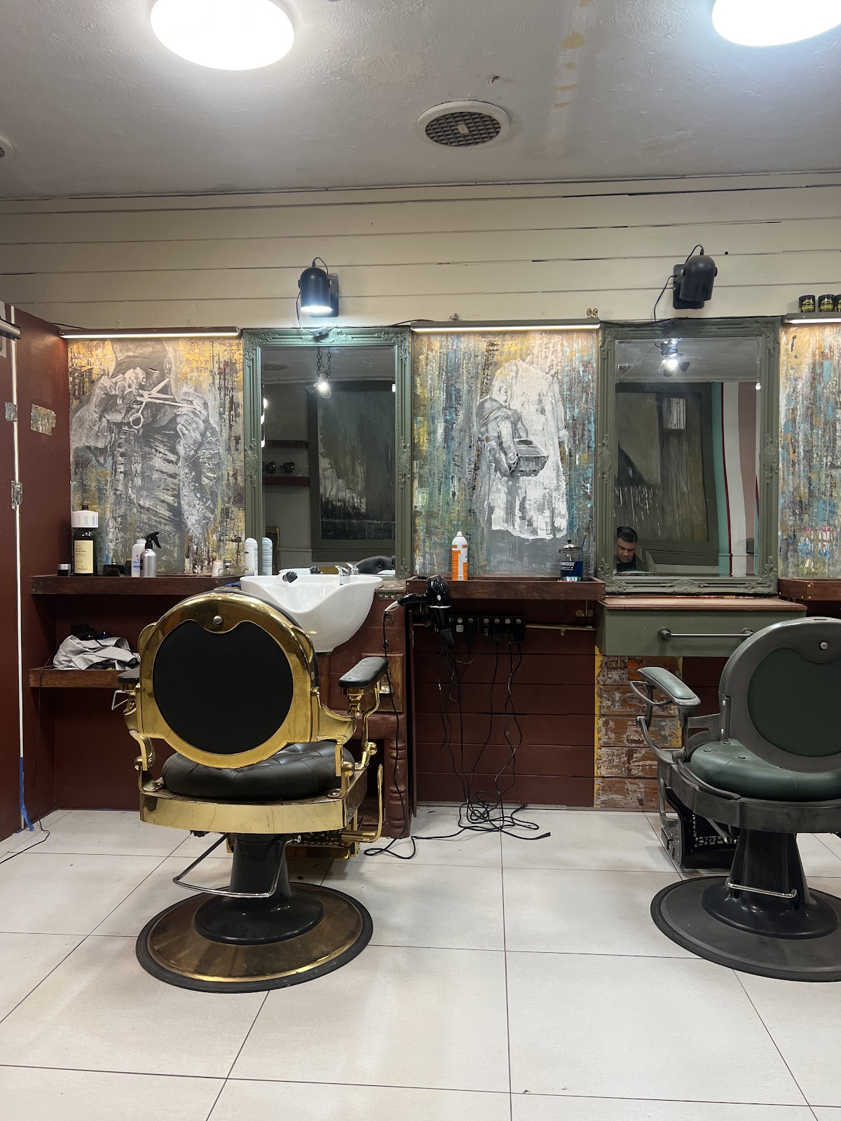 Brass antique barber chair and green chair in front of framed mirrors